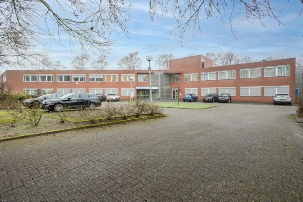 Voorgevel van een rood bakstenen kantoorgebouw aan de Christiaan Krammlaan met geparkeerde auto's op de oprijlaan.